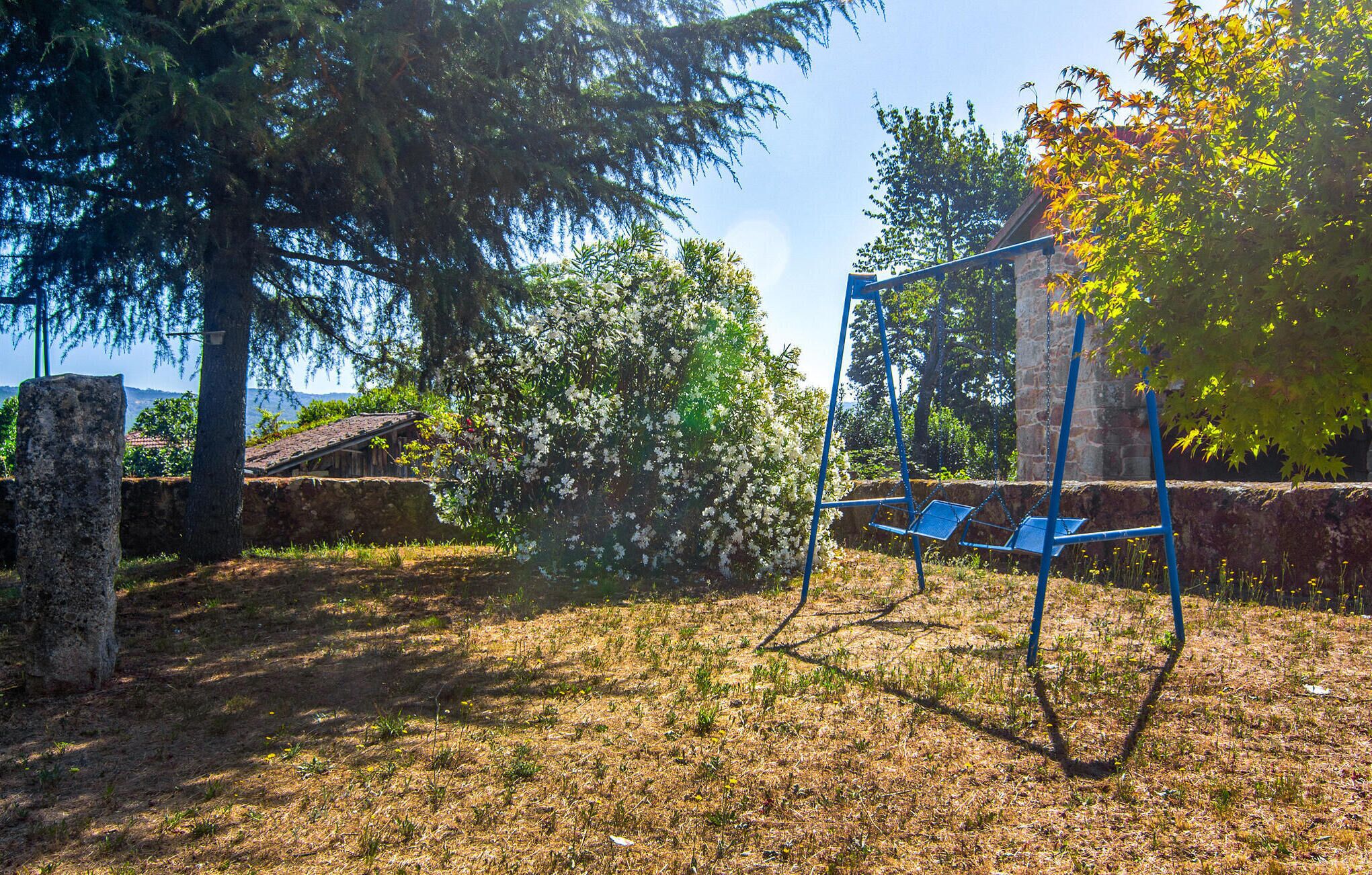 Une balançoire installée dans un espace verdoyant, avec des arbres et un mur en pierre.