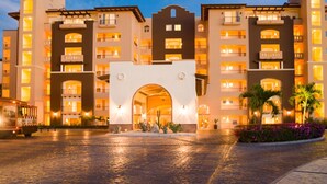 A multi-story hotel with a central archway entrance, balconies on each floor, and a paved courtyard.