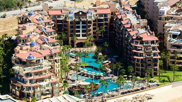 A resort with multiple buildings, a central pool area, and a beach.