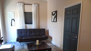 Een woonkamer met een donkerbruine bank, een bijzettafeltje met een kaars, en een deur.