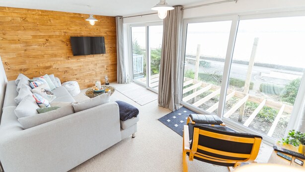 Uma sala de estar moderna com um sofá cinza, uma parede de destaque em madeira, uma TV de tela plana e vista para uma varanda com guarda-corrimão.