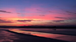 Um pôr do sol sobre águas calmas, com uma linha de costa distante.