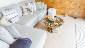 Uma sala de estar moderna com um sofá cinza, painel de parede de madeira e uma mesa de centro redonda com objetos decorativos.