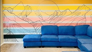 Een kamer met een blauwe modulaire bank, een bijpassend poefje en een kleurrijke abstracte muurschildering.
