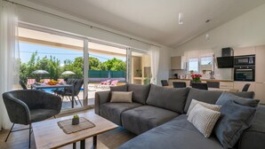 Ein modernes Wohnzimmer mit einem grauen Sofa, einem Holztisch und einem Essbereich mit Tisch und Stühlen.