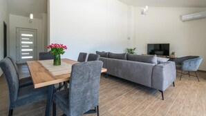 Ein modernes Wohnzimmer mit einer Couch, einem Esstisch mit Stühlen, einem Fernseher und einem Blumenstrauß.