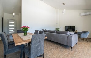 A modern living room with a sofa, a dining table with chairs, a TV, and a vase of flowers.