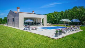 Ein modernes Haus mit Swimmingpool, Sitzgelegenheiten im Freien und einem gepflegten Rasen.
