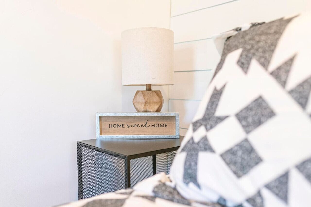 A bedside table with a lamp and a sign that reads "HOME sweet HOME".