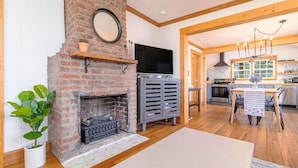 A cozy living room with a brick fireplace, a flat-screen TV, and a dining area with a wooden table and chairs.