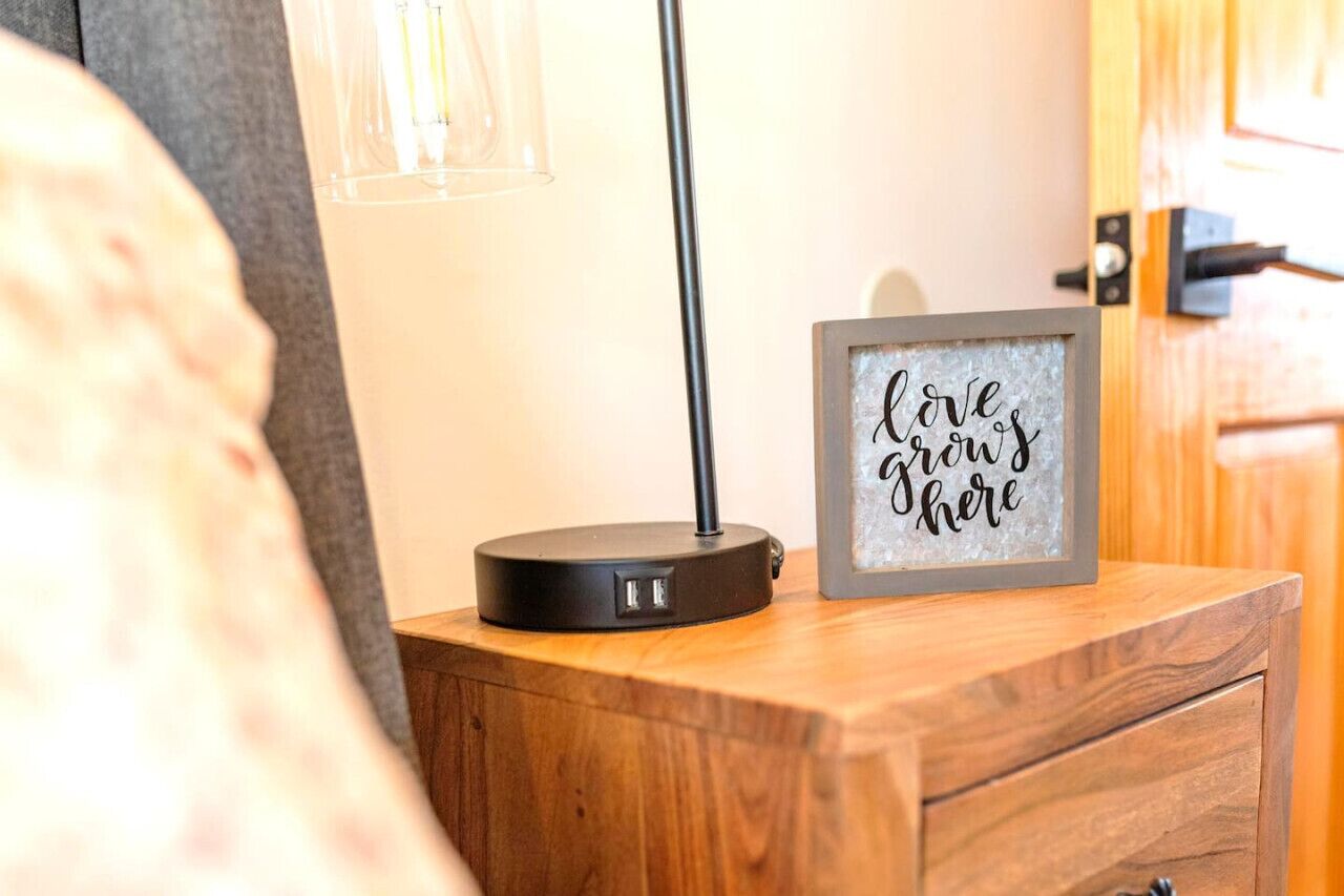A bedside table with a framed sign that reads "love grows here" and a lamp.