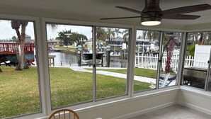 A room with large windows overlooking a marina, a dining table with chairs, and a ceiling fan. - Beautiful home on a deep water canal leading to the Gulf of America. (New Port Richey)