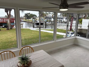 Ein Zimmer mit großen Fenstern mit Blick auf eine Marina, einem Esstisch mit Stühlen und einem Deckenventilator.