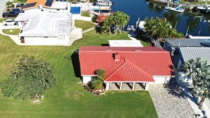 An aerial view of a residential area with a house featuring a red roof, a covered patio, and a lawn. - Beautiful home on a deep water canal leading to the Gulf of America. (New Port Richey)