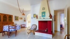 Un salon doté d’une cheminée, d’une table à manger, de chaises en osier et de différents éléments décoratifs sur les murs.