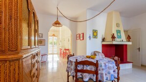 Un coin repas avec une table et des chaises en bois, un luminaire suspendu et un mur rouge agrémenté d’objets décoratifs.