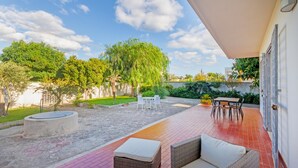 Une terrasse avec des meubles d’extérieur, une table ronde et des chaises. On aperçoit un arbre et un mur au fond.