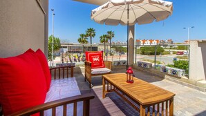 Ein Balkon mit Holztisch und -stühlen, einem roten Kissen und einem großen Sonnenschirm.