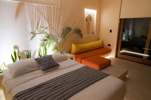 A modern bedroom with a bed, a small orange sofa, and a large window with a view. - Tikul Hotel Boutique (Isla Holbox)