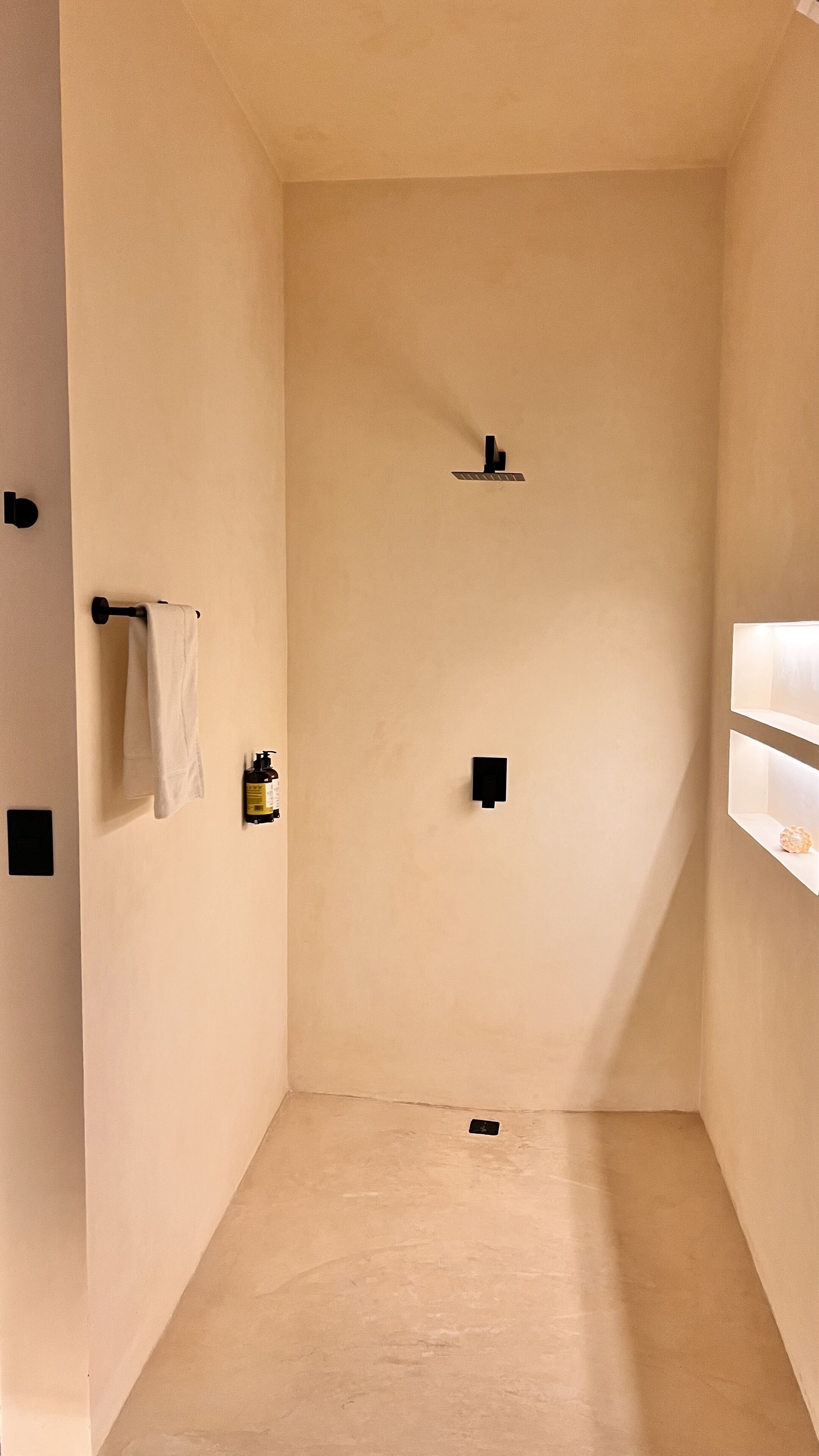 Un baño minimalista con una toalla colgada en un perchero, un dispensador de jabón y una pequeña estantería con una botella.