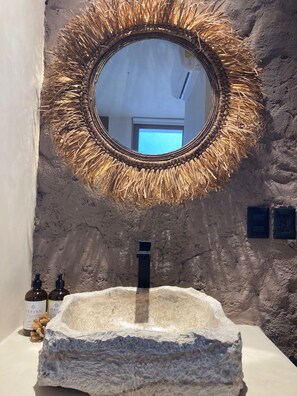 A bathroom with a stone sink, a mirror with a straw-like frame, and a view of the outside. - Tikul Hotel Boutique (Isla Holbox)