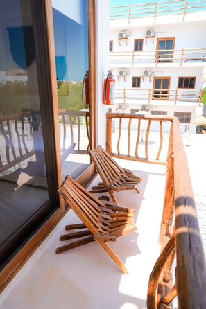 A wooden deck with a railing, a fire extinguisher mounted on the wall, and a view of a building with multiple windows and balconies. - Tikul Hotel Boutique (Isla Holbox)