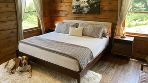 Ein Schlafzimmer einer Holzhütte mit einem Bett, einem Nachttisch, einem Hund und einem Gemälde an der Wand.