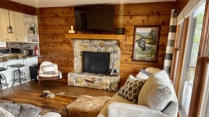 Ein gemütliches Blockhaus-Interieur mit Kamin aus Stein, Holzwänden, einem Fernseher und einem gerahmten Bild einer Motorrad.