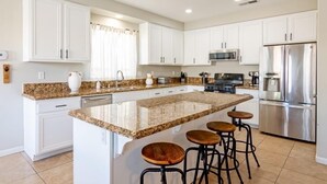 Eine moderne Küche mit weißen Schränken, Granit Arbeitsplatten, einem Edelstahlkühlschrank und einer zentralen Kochinsel mit Barhocker.