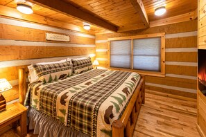 A cozy log cabin bedroom with a large bed, a window with blinds, and a wooden ceiling.