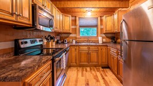 A kitchen with wooden cabinets, stainless steel appliances, granite countertops, and a window with blinds. - True Log Cabin W/ ⛰Stunning Views⛰, Hot Tub, Sauna, Pool Table (Gatlinburg)