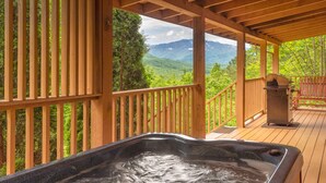 A wooden deck with a hot tub, a grill, and a view of mountains. - True Log Cabin W/ ⛰Stunning Views⛰, Hot Tub, Sauna, Pool Table (Gatlinburg)