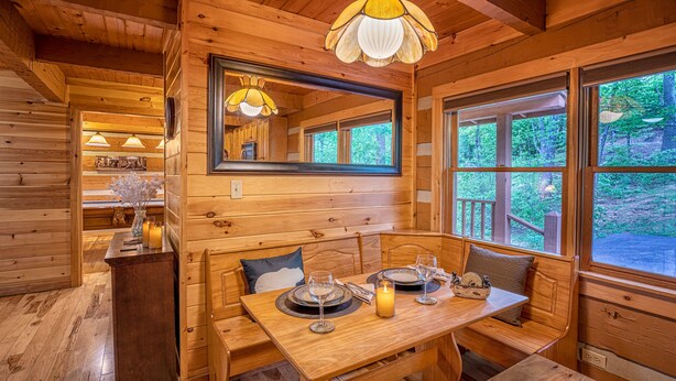 A wooden cabin interior with a dining table set for two, a bench, and a mirror above the table. - True Log Cabin W/ ⛰Stunning Views⛰, Hot Tub, Sauna, Pool Table (Gatlinburg)
