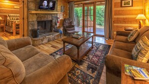 A cozy cabin interior with a stone fireplace, wooden furniture, and a television mounted above it. - True Log Cabin W/ ⛰Stunning Views⛰, Hot Tub, Sauna, Pool Table (Gatlinburg)