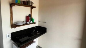 A compact kitchen with a built-in oven, a small refrigerator, and a shelf with kitchenware. - Beautiful Dendê Chalet 5 min from Corumbau Beach (Prado - Corumbau)
