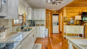 Una cocina compacta con armarios blancos, encimera de mármol y suelo de madera.