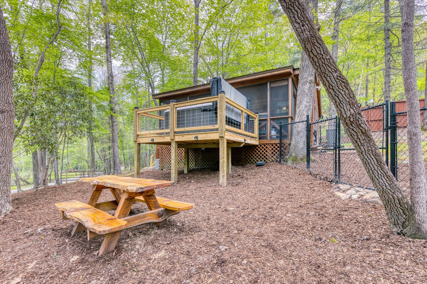 Eine Holzterrasse mit Picknicktisch, umgeben von Bäumen und einer Hütte mit Balkon.