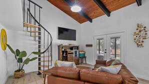 A spacious living area with a brown leather sofa, a wooden staircase, and a flat-screen TV mounted on the wall. - Modern Lakefront Loft Retreat ~ Private Beach & Water Toys (Little Elm)