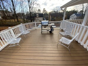 Une terrasse en bois avec des chaises en métal blanc et un barbecue.