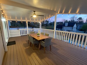 Une terrasse extérieure couverte, dotée d’une table et de chaises en bois, d’un ventilateur de plafond et de guirlandes lumineuses.