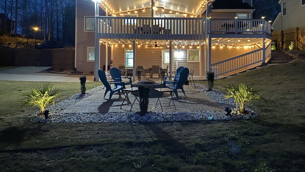 Una casa de dos pisos con un porche cubierto, mobiliario exterior e iluminación colgante.