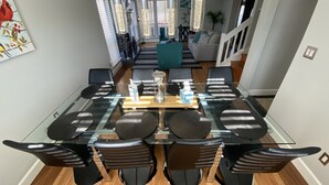 Un comedor moderno con una mesa de vidrio, sillas negras y lámparas colgantes.