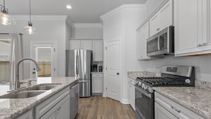 A modern kitchen with white cabinetry, stainless steel appliances, granite countertops, and a wood floor. - Brand New Modern Farmhouse (Shreveport)