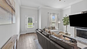A living room with a brown leather sofa, a flat-screen TV, and a fireplace. - Brand New Modern Farmhouse (Shreveport)