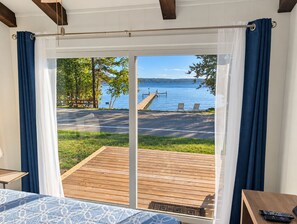 A room with a large sliding glass door leading to a deck with a view of a lake and dock.