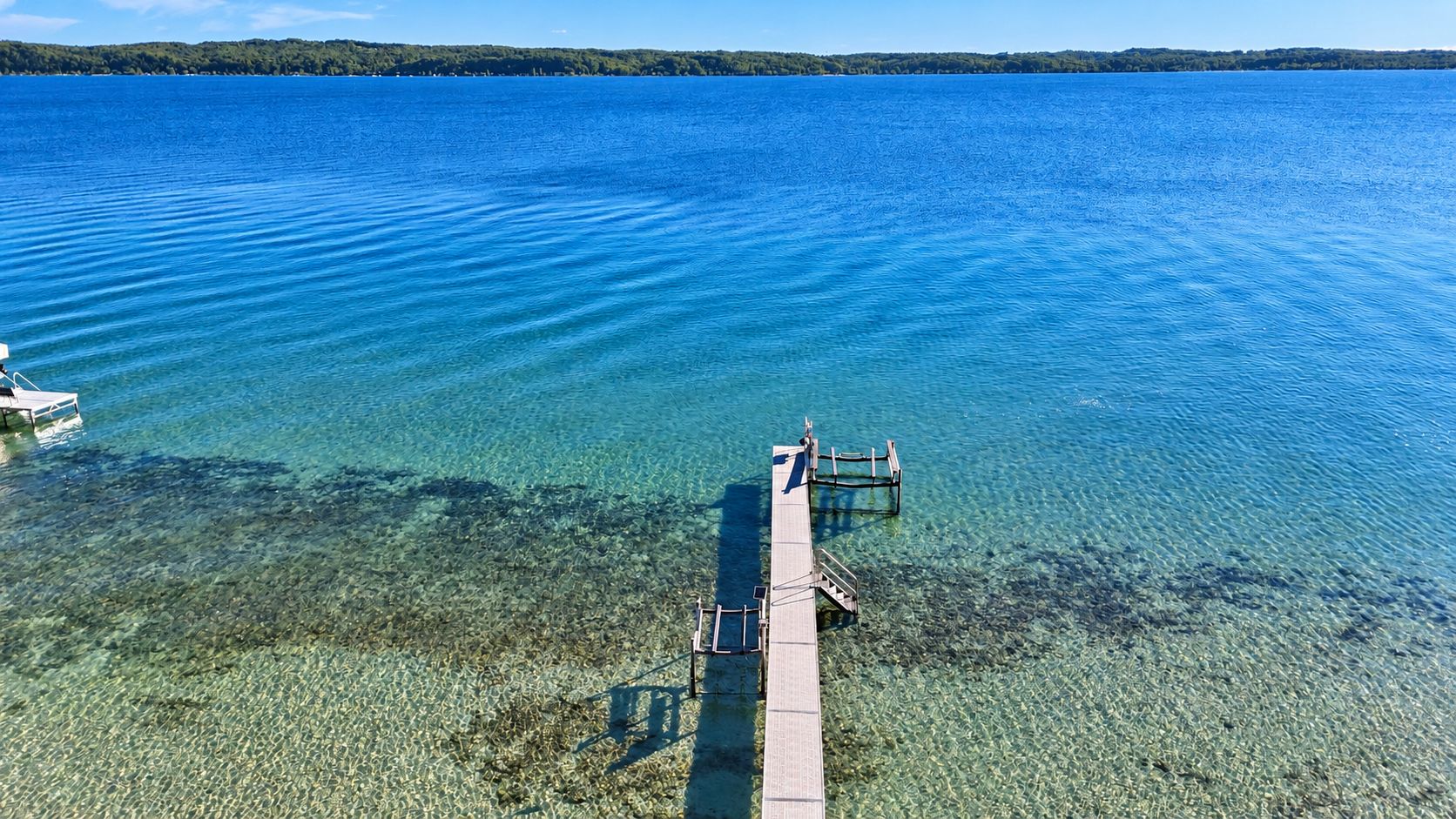 Vista despejada de un lago con un muelle que se adentra en el agua, un pasillo de madera y un bote pequeño a la izquierda.