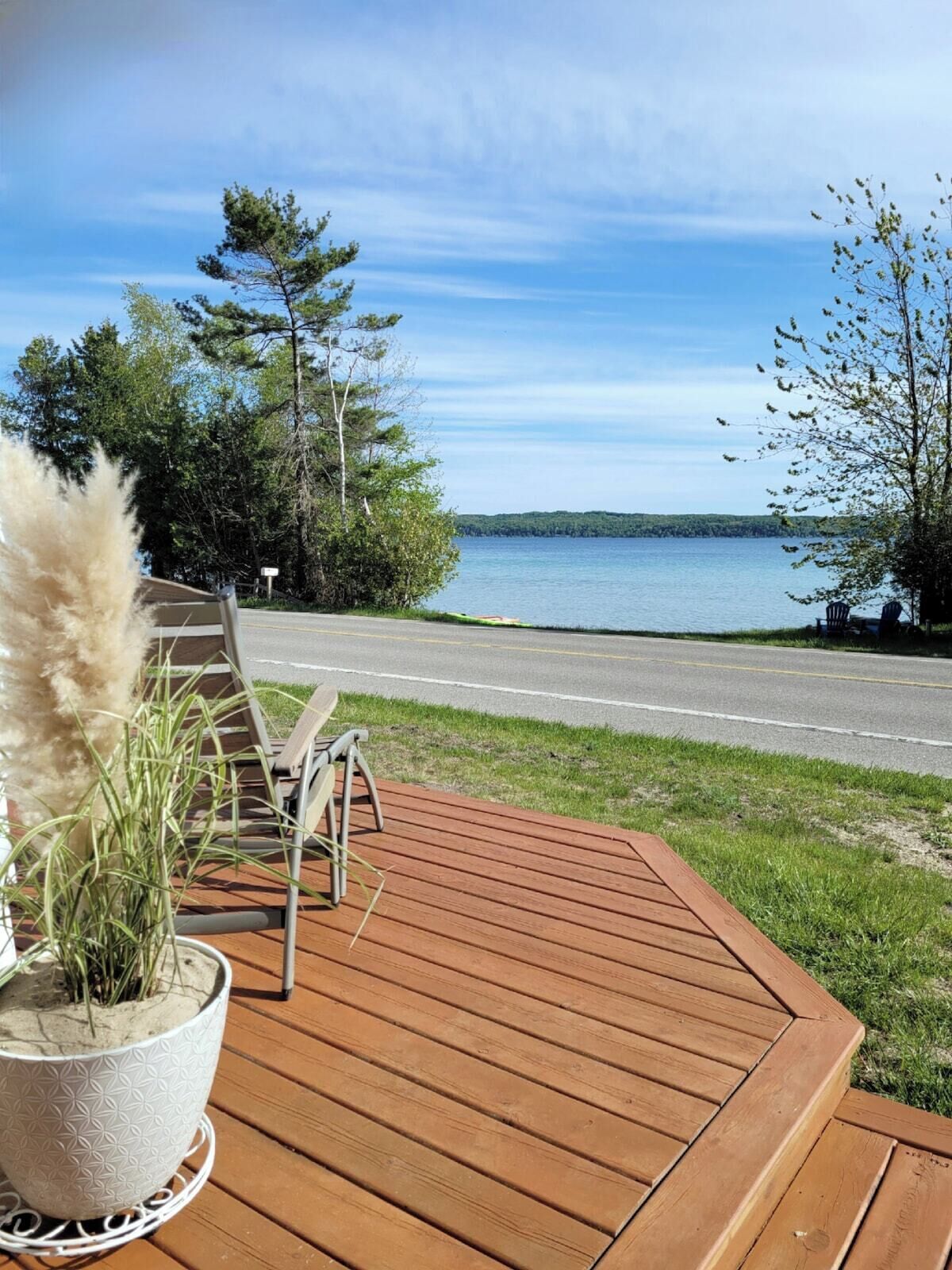 En træterrasse med en potteplante, to stole og udsigt til et sø og en vej.