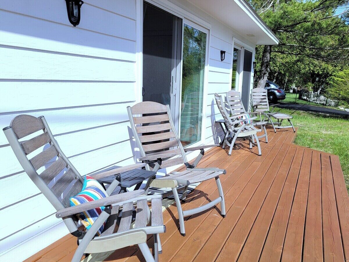 A deck with four lounge chairs and a table, a sliding glass door, and a house with white siding.