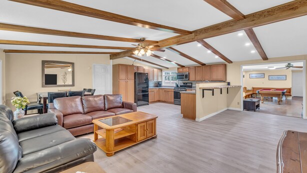 Amplia sala de estar con sofá de cuero, mesa de centro de madera y una mesa de comedor. La cocina cuenta con gabinetes de madera y una isla central.