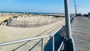 Un paseo marítimo de madera con barandillas metálicas que conduce a una zona de playa arenosa.